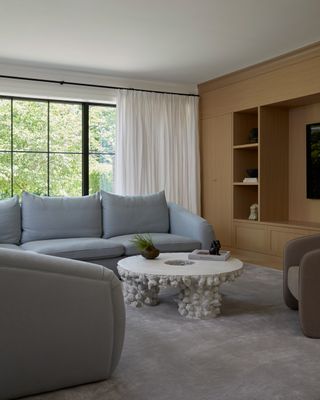 neutral living room with light blue sofa, sculptural coffee table, and timber cabinetry