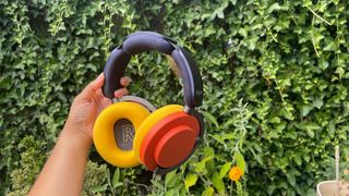 Dyson OnTrac wireless headphones in hand in yellow and red option against garden hedge