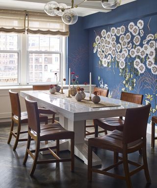 A dining room wall idea with a deep blue wallpaper with non-repeating white flower design and brown leather dining chairs