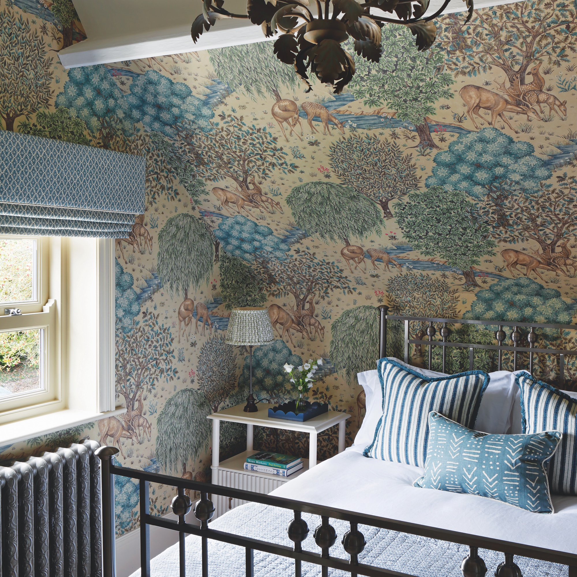 bedroom with pitched roof and beams, with forest scene wallpaper and iron bedstead