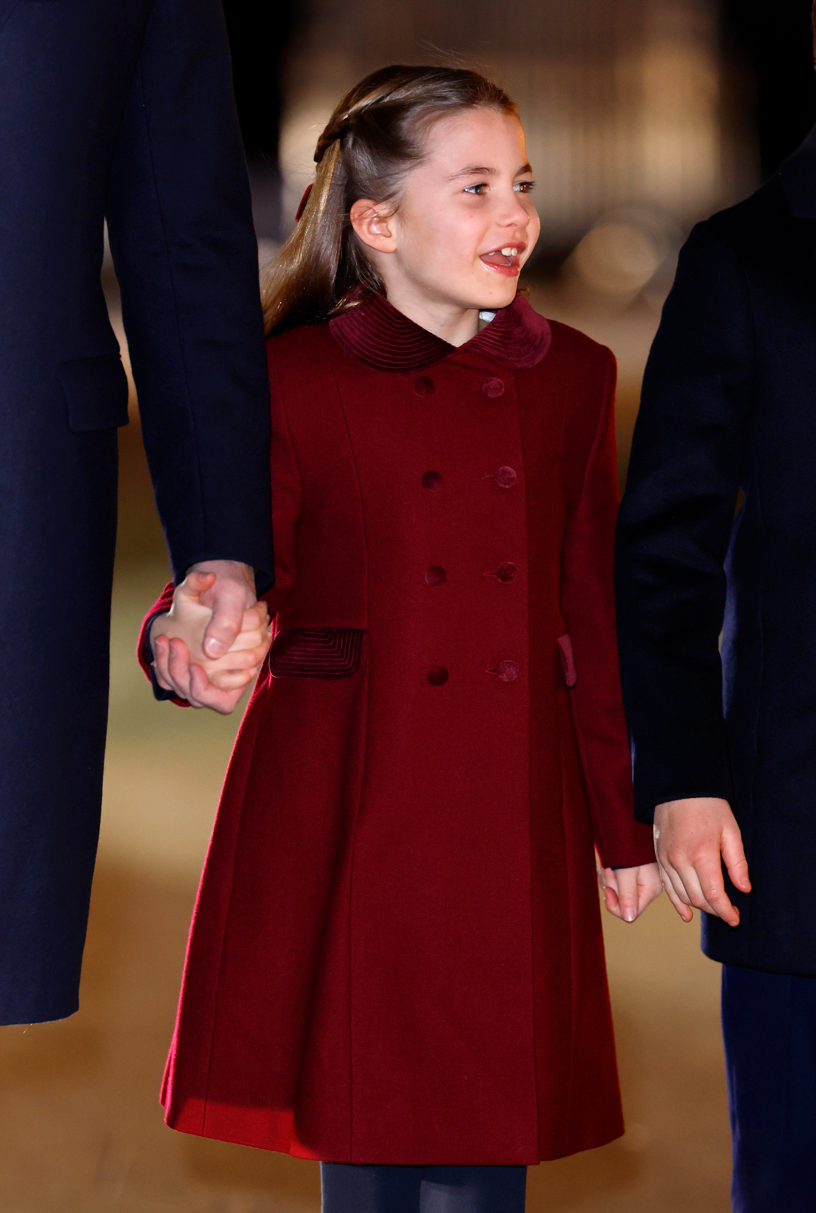 Princess Charlotte wearing a burgundy coat and smiling holding Prince William&#039;s hand