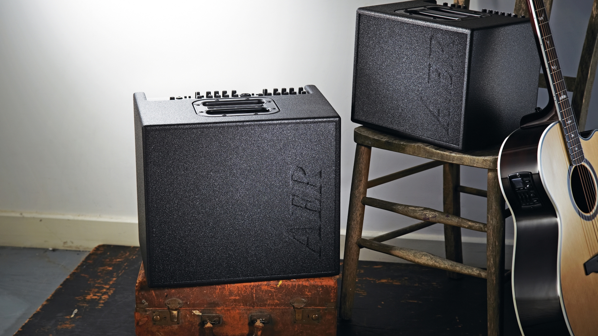 Two AER acoustic guitar amps on stools with an acoustic guitar