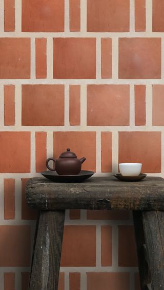 A red tiled wall with chunky grouting, and a small wooden side table in front