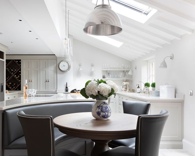 An example of kitchen extension trends showing an open plan white kitchen with a round table with black chairs and flowers on it