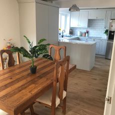 Kitchen diner with light grey units, white marble look worktops, warm oak flooring and a warm wood dining table