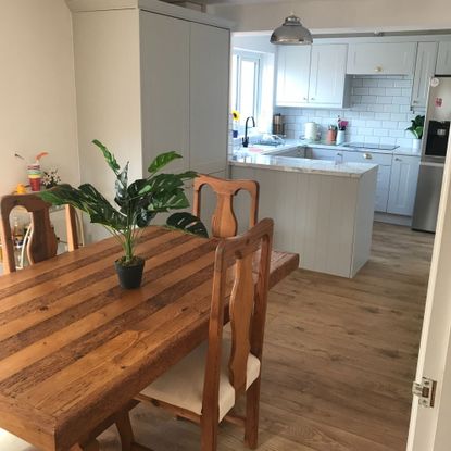 Kitchen diner with light grey units, white marble look worktops, warm oak flooring and a warm wood dining table