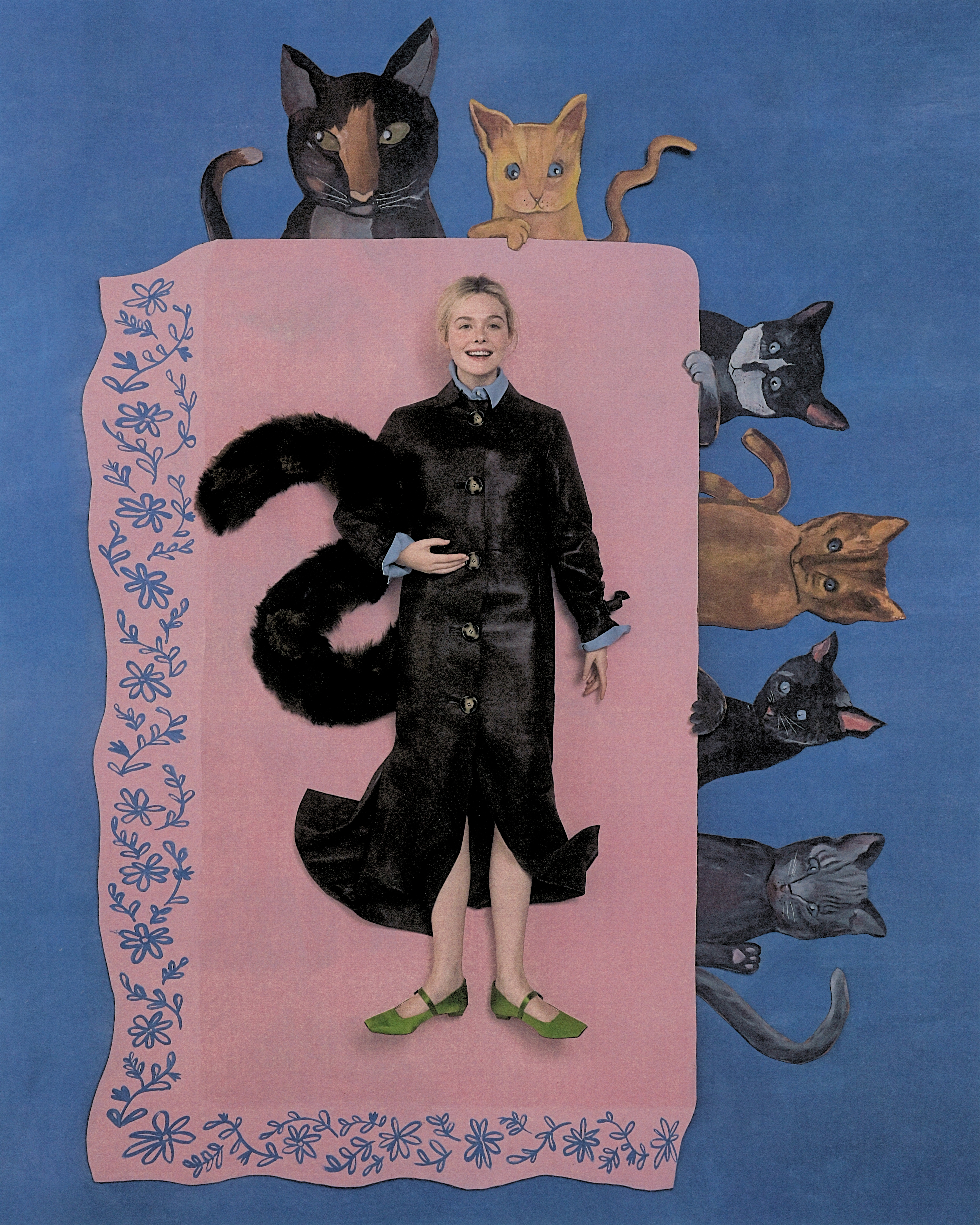 Elle Fanning shot by Szilveszter Mak&amp;oacute;. She is lying flat on a table made of painted cardboard. The tablecloth is pink with painted flowers on the border. Sitting around the table are cutout cats made of painted cardboard. Fanning is wearing a long, buttoned leather coat with green Mary Jane flats. She is holding a faux fur scarf styled like a cat tail.