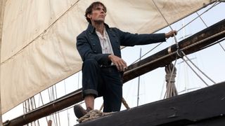 Edmond (Sam Claflin) stands on his ship in calm weather, with his left arm leaning on a rope attached to the main sail, and his right arm resting on his right leg, which is propped up on the side of the ship.