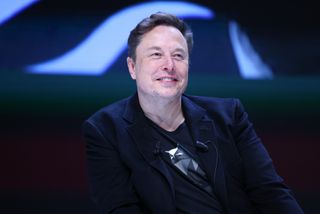 a man in a black blazer over a black t-shirt smiles on stage at a press event