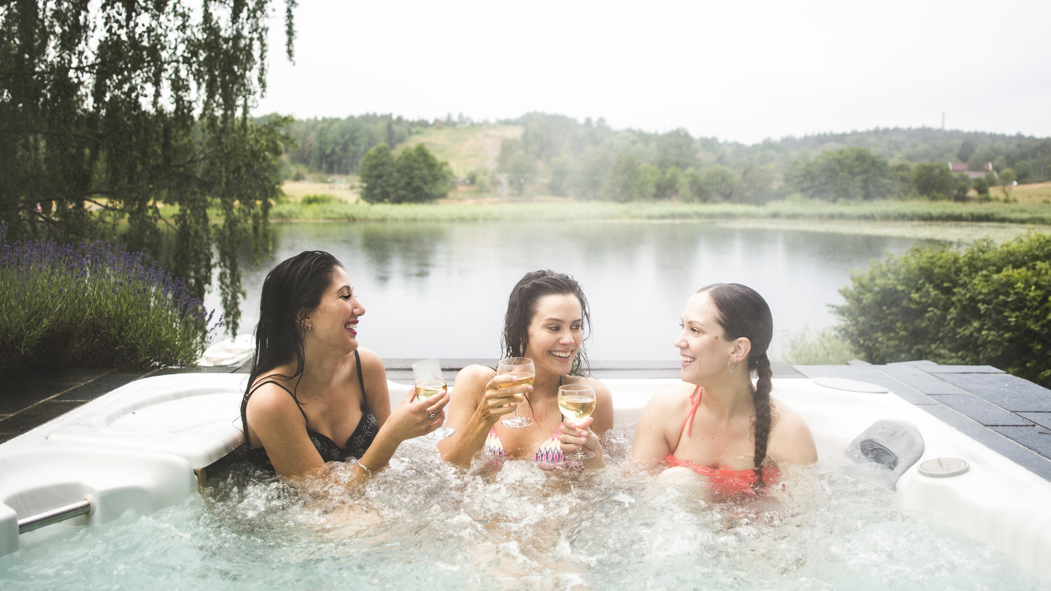 Best hot tubs: Three women relax and drink champagne in a hot tub overlooking a lake