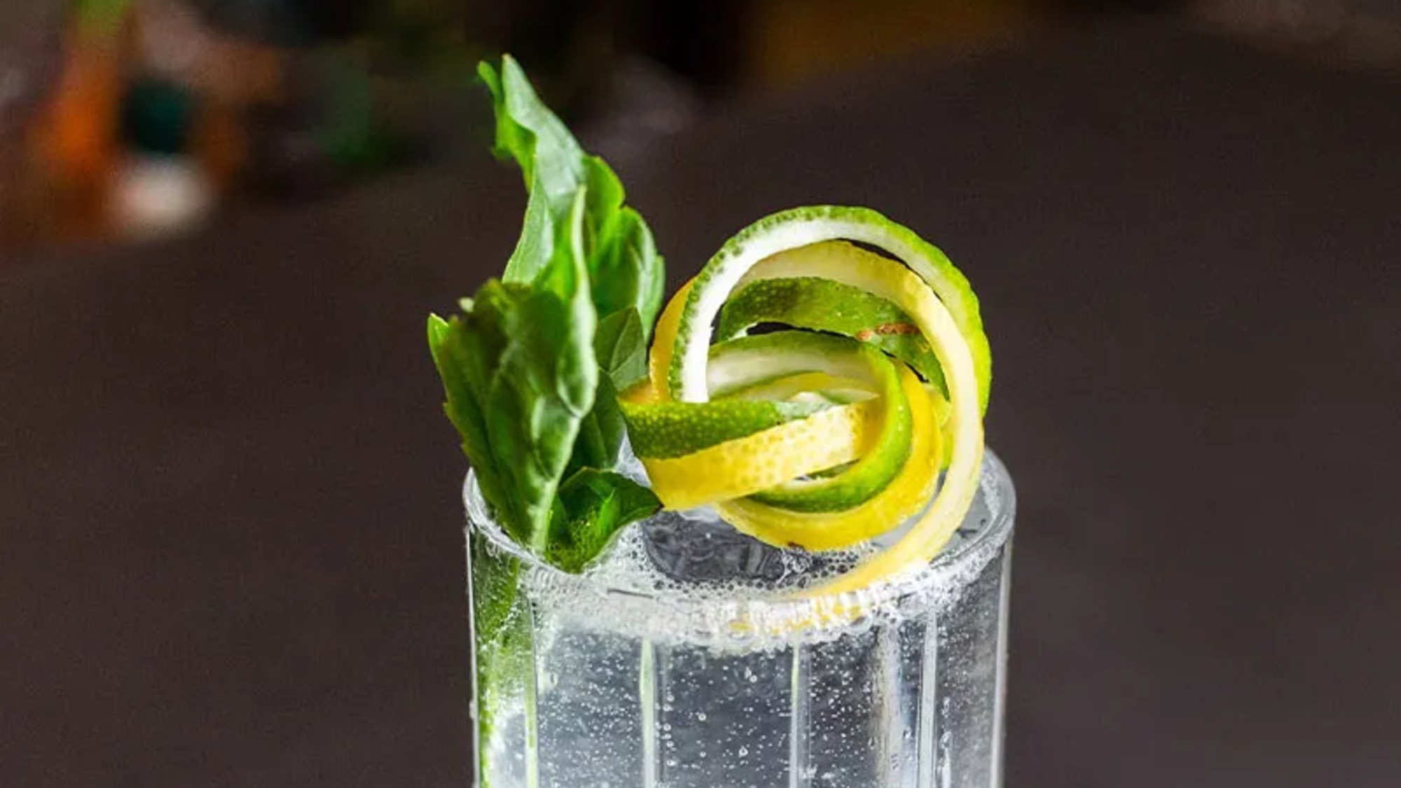 3/4 angle shot of the top of a gin rickey, with a garnish of a basil lead and a tangle of lime and lemon zests