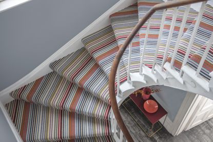 View of curved staircase carpet ideas from above with grey wall and striped carpet