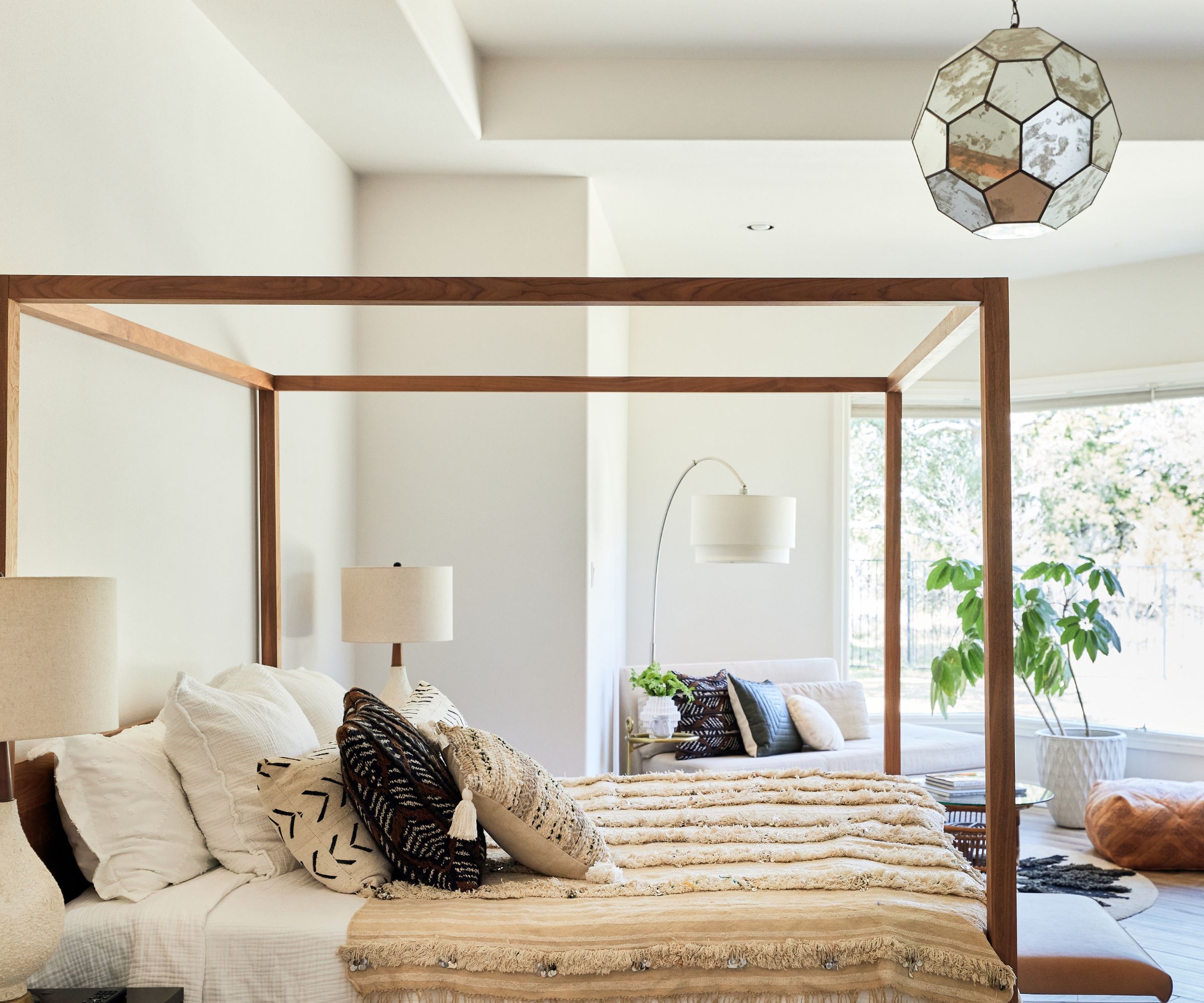 bedroom with minimalist four poster bed chaise longue white walls and big window