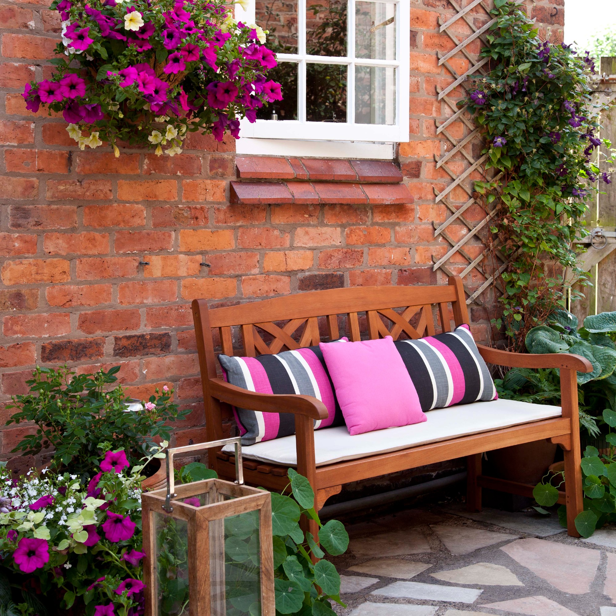 A patio with a garden bench with pink cushions surrounded by flowers