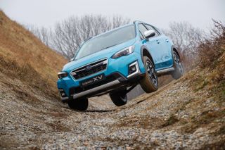 Daytime outside image of a blue XV E-Boxer Subaru plug-in hybrid on rugged terrain, bare trees in the backdrop