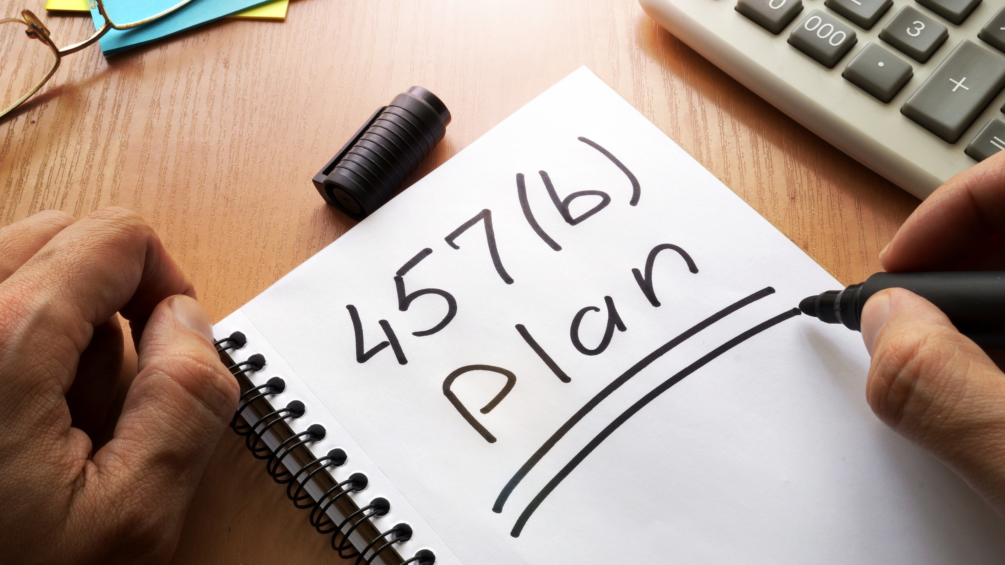 The words "475(b) plan" written on a spiral notepad next to a calculator.