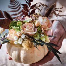 hands holding a small pumpkin filled with flowers