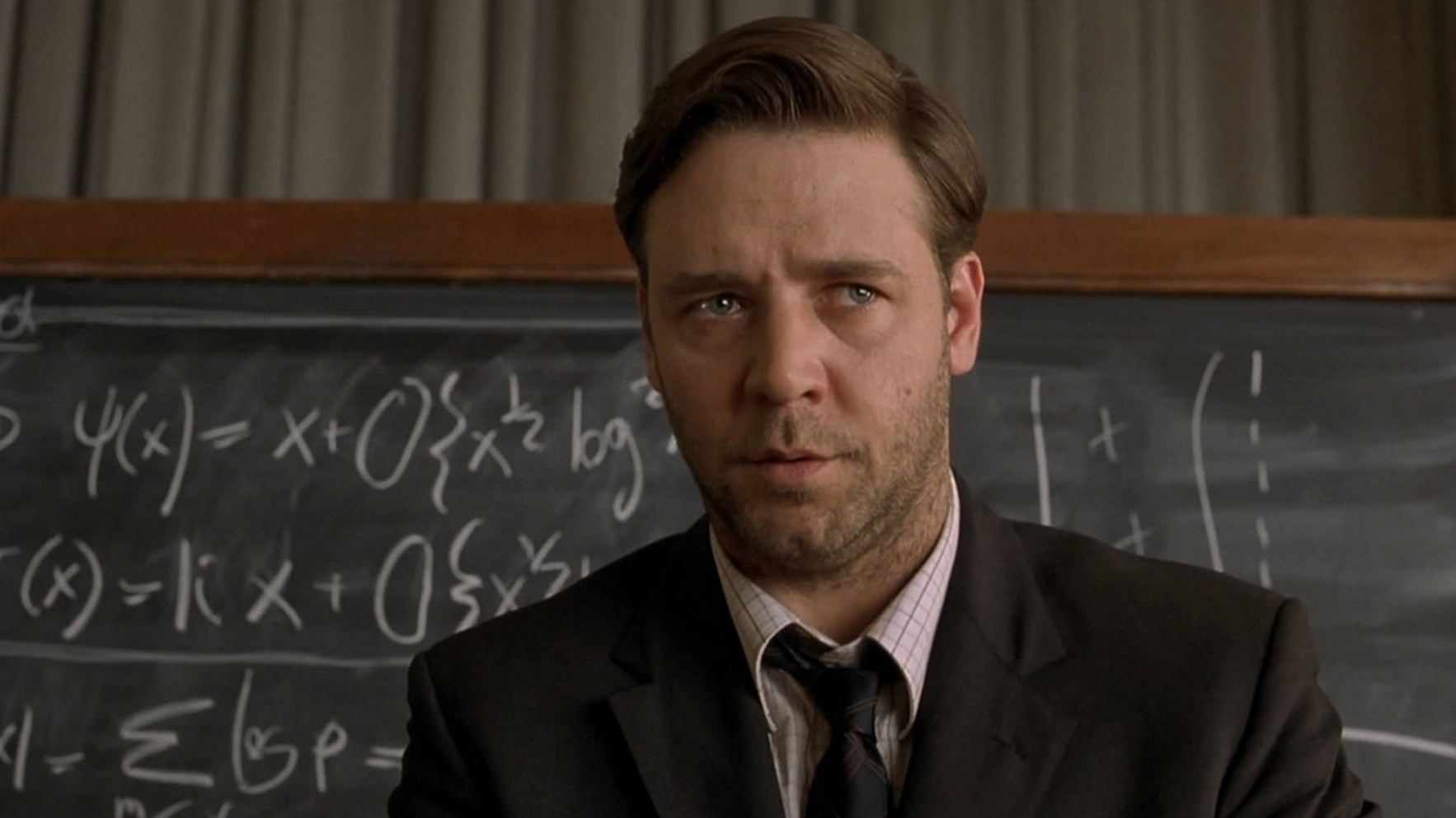 A still from the movie A Beautiful Mind, a close-up of Russell Crowe with a blackboard in the background