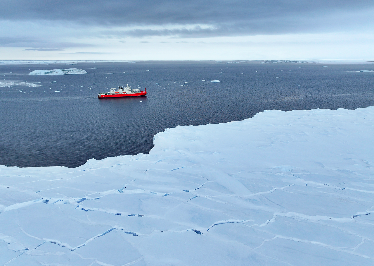 Large Antarctic ice sheet viewed from above with expedition boat in the distance.