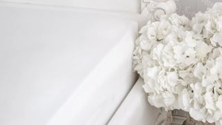 white best sheets on bed next to white hydrangea in a vase on bedside table