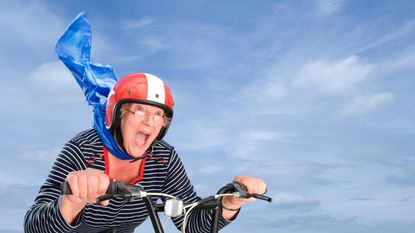 A woman happily rides a bike with her scarf blowing in the wind.