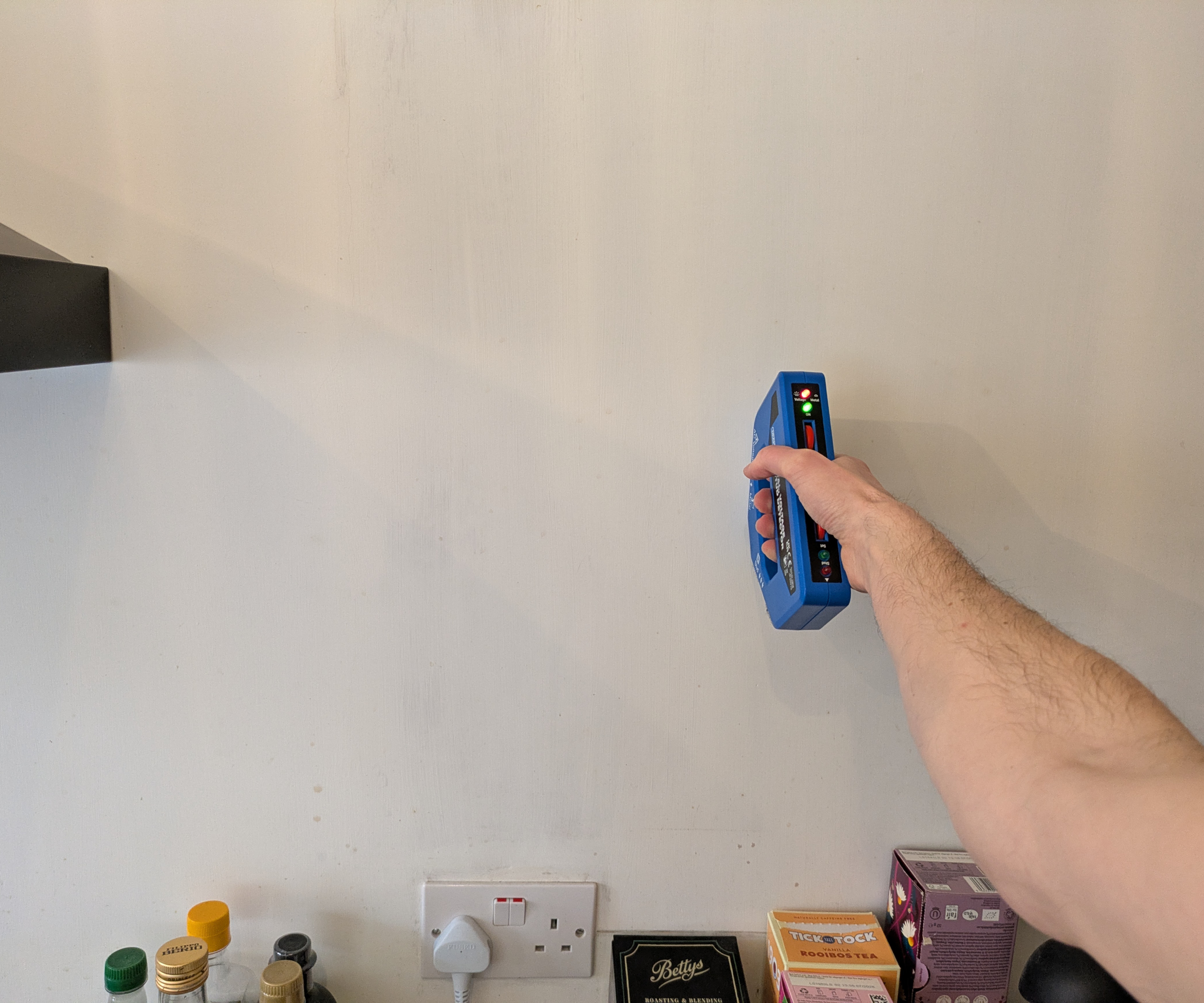 A person holding a wire detector against a wall