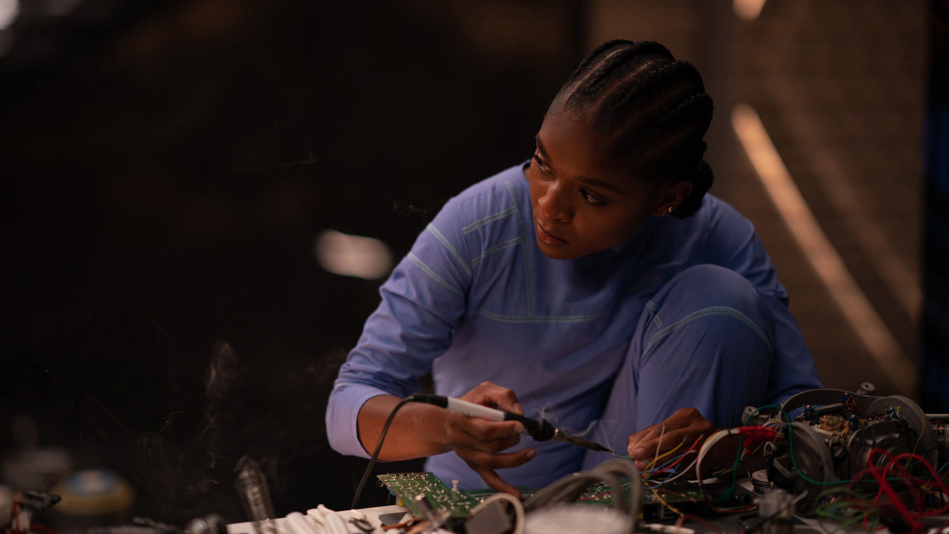 Riri Williams looks up from working on her Ironheart suit at a bench in Black Panther: Wakanda Forever