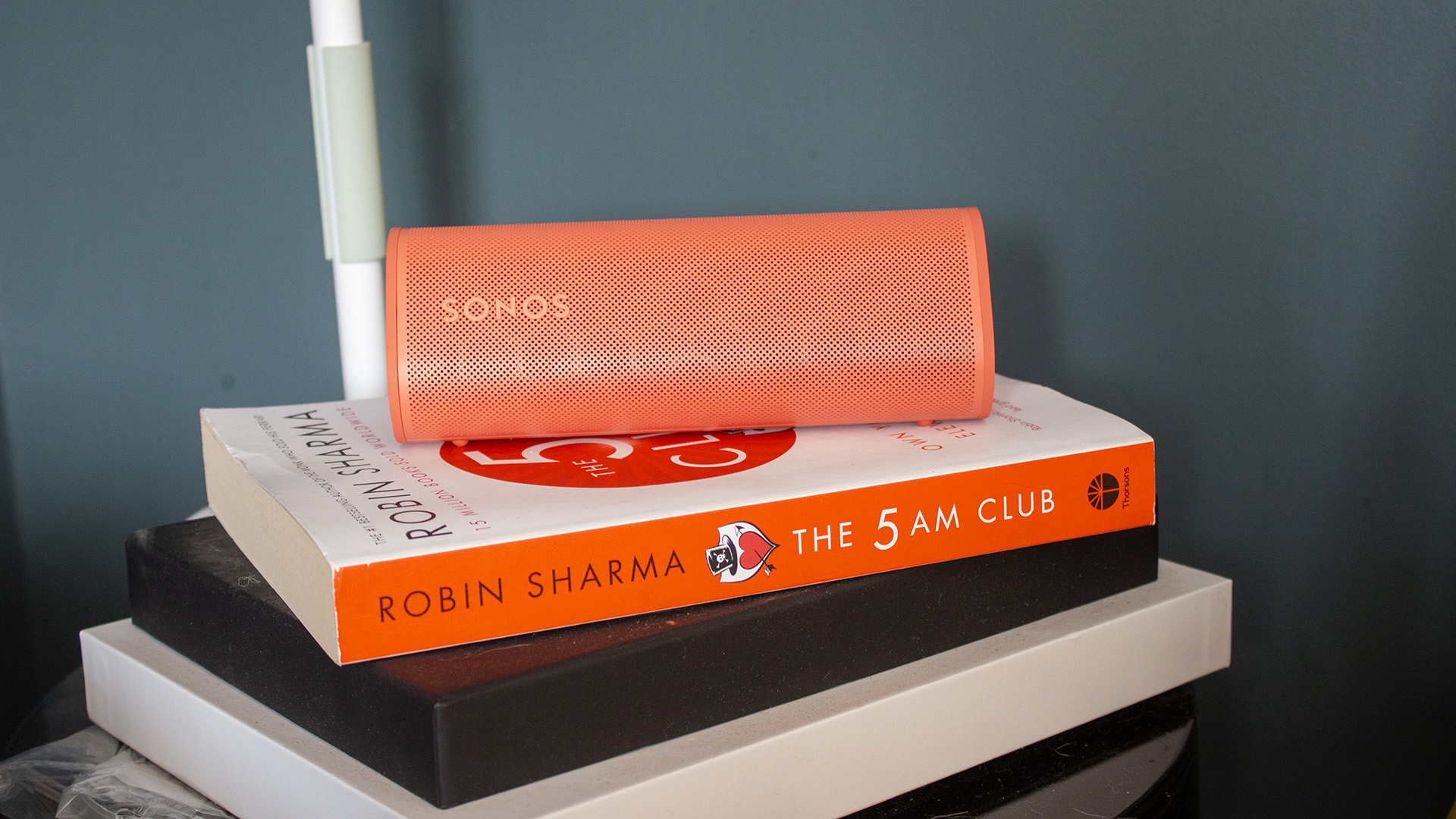 a red sonos roam 2 speaker in a living room on top of a red book
