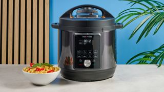 a black instant pot with a dial and touchpad is photographed against a blue background