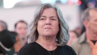 Rosie O'Donnell with shoulder-length gray hair standing in a crowd in Hacks Season 4
