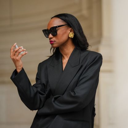 street style shot of woman in black blazer holding perfume bottle