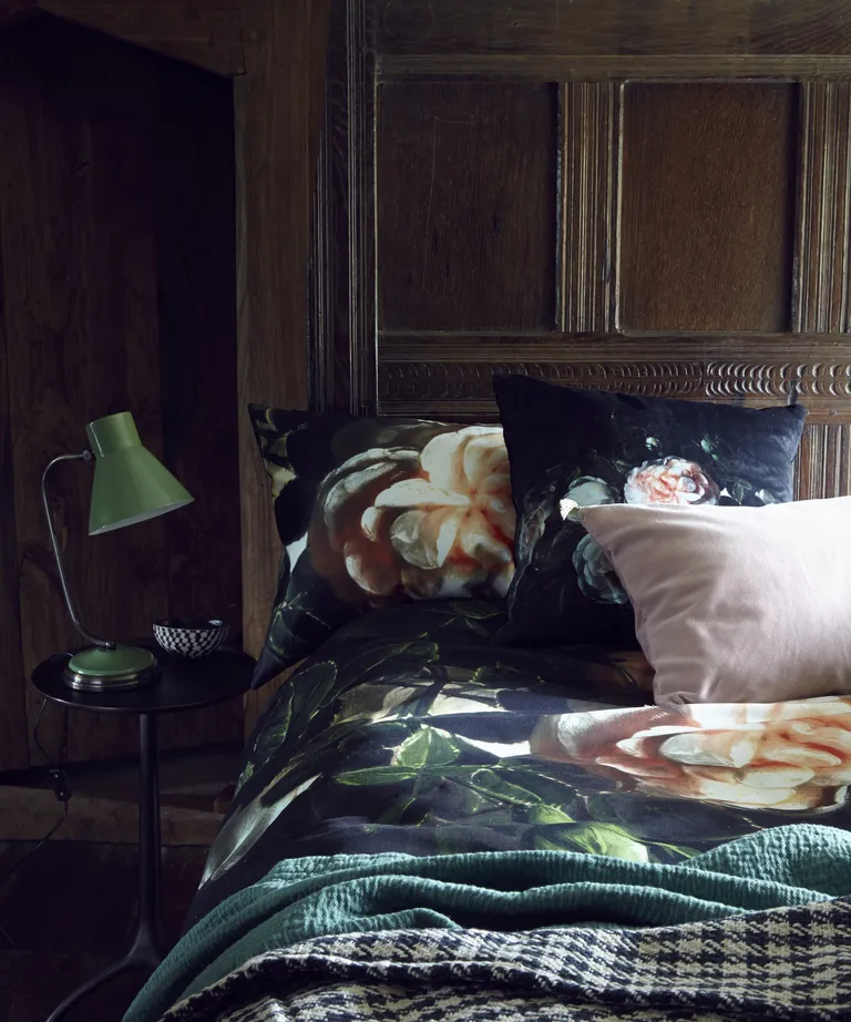 A bedroom with wood panelled walls, and dark green silk bedding