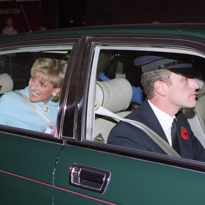 Princess Diana wearing a blue suit waving from a green car as her chauffeur drives her