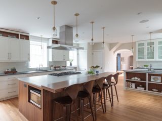 white and walnut kitchen with breakfast bar on kitchen island, bar stools, white cabinetry, glass pendant lights, open shelving