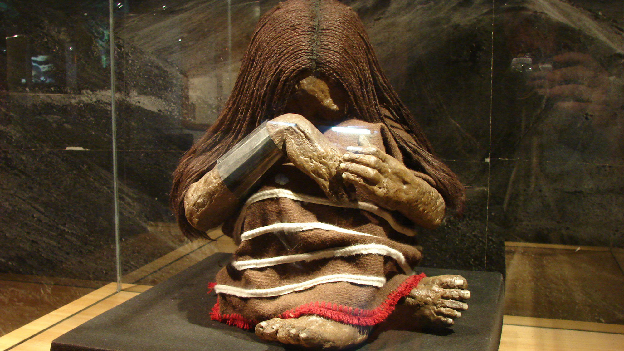 A reconstruction of a body clutching his knees with various colored cords wrapped around them is on display