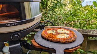A cooked pizza on a peel beside the Gozney Arc XL pizza oven