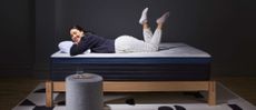 The Helix Midnight Luxe mattress review image shows a dark-haired woman wearing grey jogging bottoms and a black jumper laying on her stomach on top of the mattress