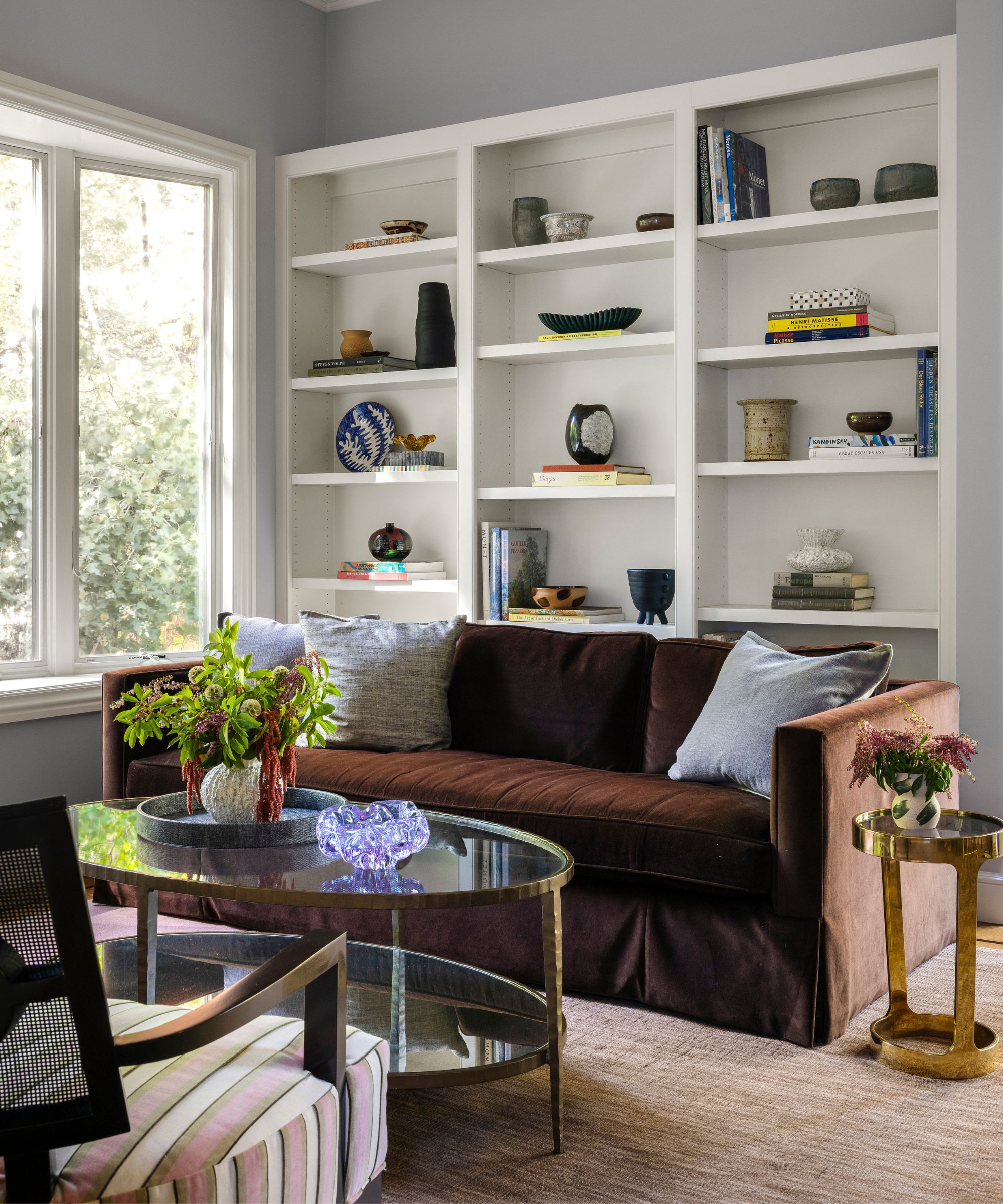 A modern living room with a dark brown sofa, white shelving, and gray walls.
