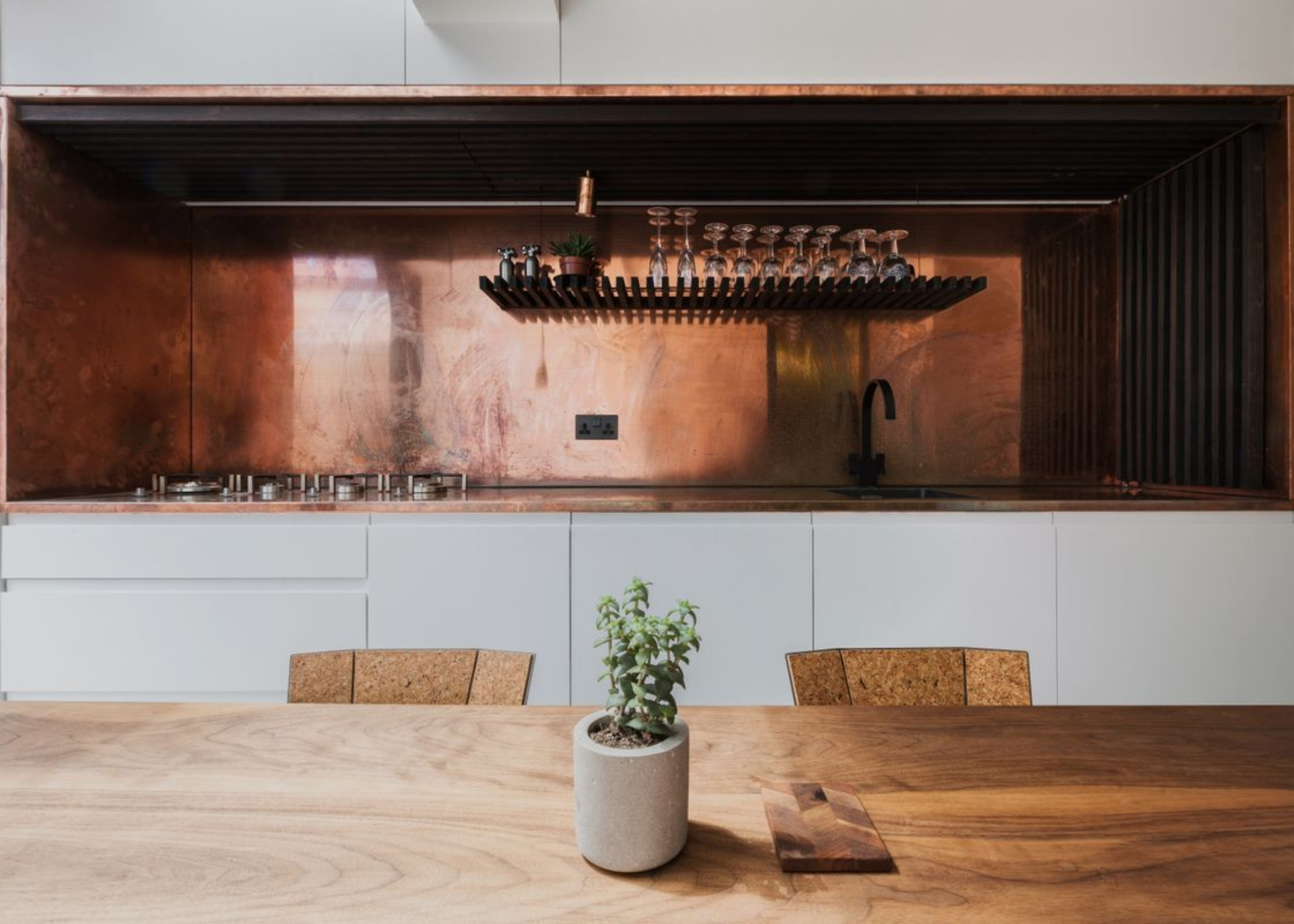 Copper kitchen by Studio 304 with a dining table in the middle and a plant pot on top