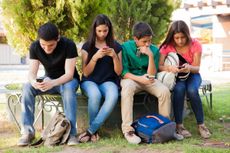 Group of teenage boys and girls ignoring each other while using their cell phones at school.