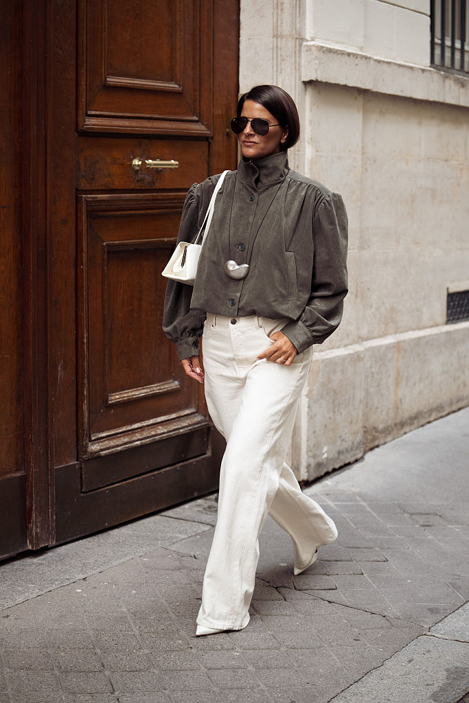 A guest wears a funnel neck jacket and white jeans to Paris Fashion Week