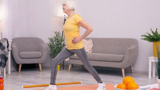 Older woman in t-shirt and leggings doing a lunge exercise at home in living room