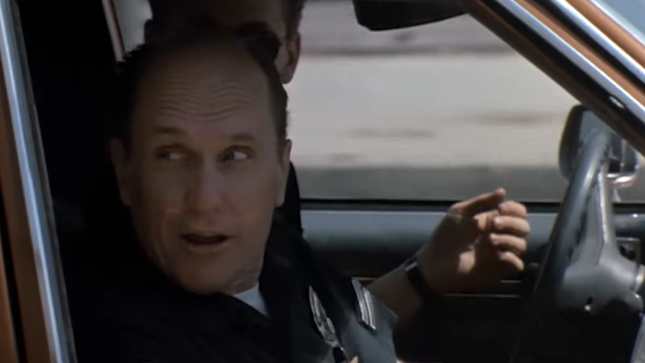 Robert Duvall in a car, wearing a police uniform and looking over his shoulder in Colors.