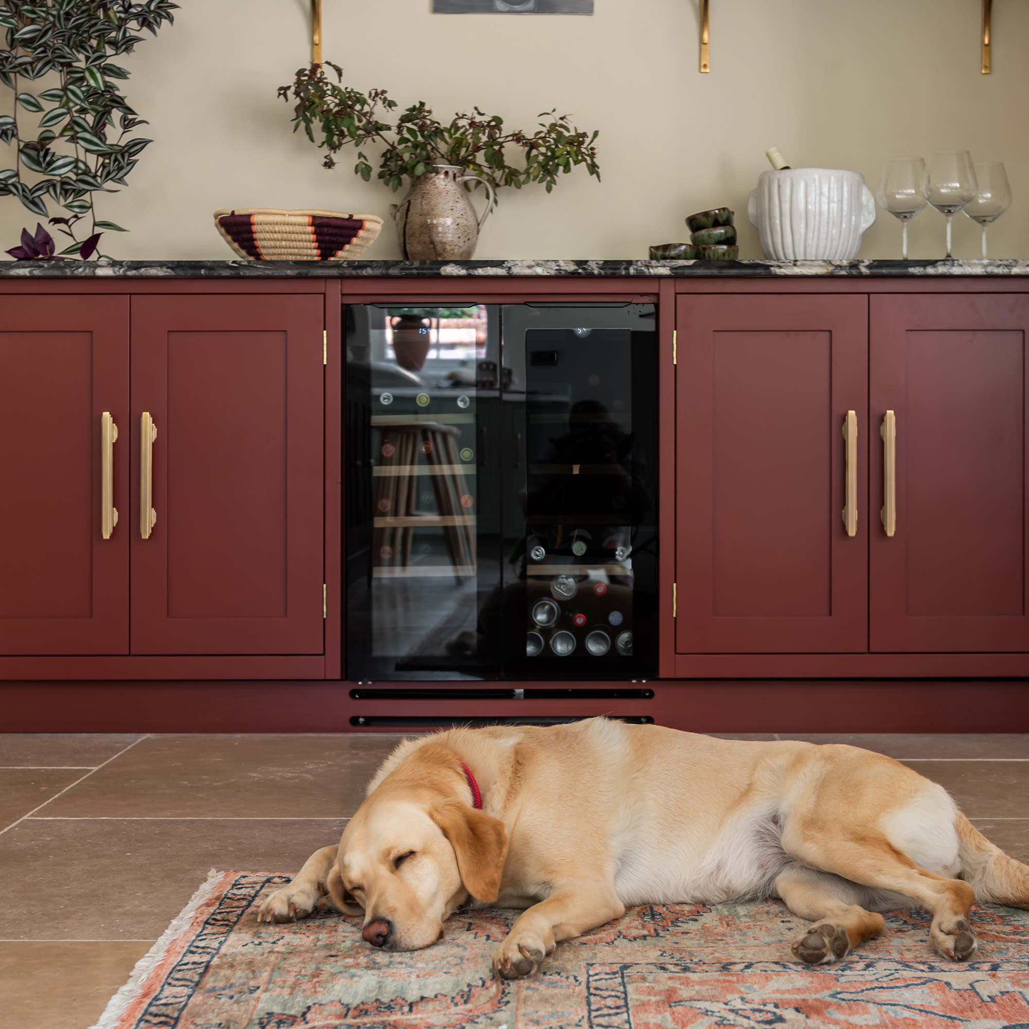 utility space in kitchen with red cabinetry and wine fridge with stone floors and dog sleeping on the rug
