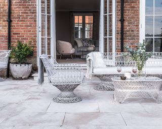 How much does a patio cost, illustrated with high end natural stone pavers in front of a brick house with modern white metal garden furniture.