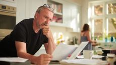 Mature man looks at paperwork standing at the kitchen counter