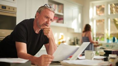 Mature man looks at paperwork standing at the kitchen counter