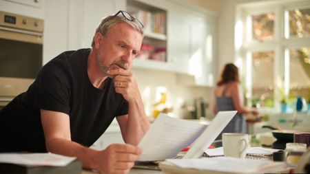 Mature man looks at paperwork standing at the kitchen counter