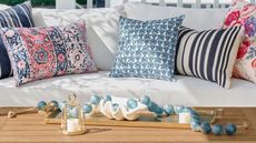 Pottery Barn outdoor white cushioned couch with multicolored blue and pink outdoor pillows next to a wooden table with coastal decor 