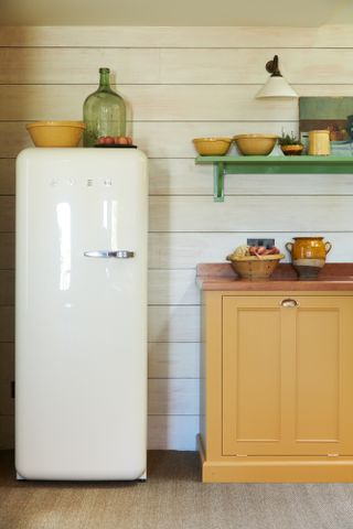 classic fridge, cream, horizontal wooden wall panelling, yellow cabinet and bowls, green shelf and jar